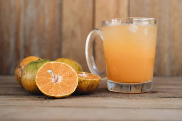 Bicchiere di succo di mandarino fresco con mandarini maturi sullo sfondo di legno — Foto Stock