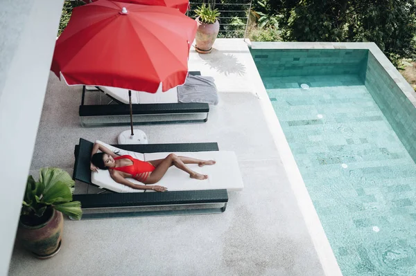 Sexy femme asiatique dans un maillot de bain rouge posé dans un transat au bord de la piscine — Photo