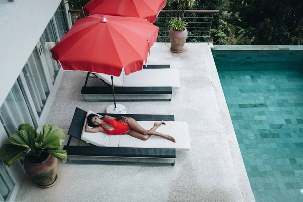 Sexy femme asiatique dans un maillot de bain rouge posé dans un transat au bord de la piscine — Photo