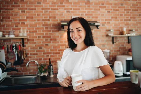 Genç ve mutlu bir kadın sabahları mutfakta kahve içiyor..