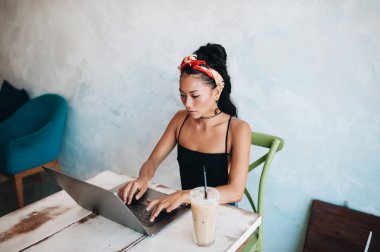 Kafede dizüstü bilgisayarı ve kahvesiyle çalışan Asyalı kadın