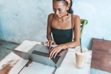 Kafede dizüstü bilgisayarı ve kahvesiyle çalışan Asyalı kadın