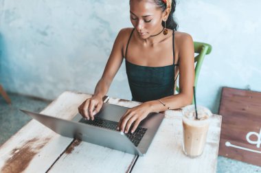 Kafede dizüstü bilgisayarı ve kahvesiyle çalışan Asyalı kadın