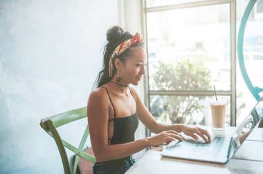 Kafede dizüstü bilgisayarı ve kahvesiyle çalışan Asyalı kadın