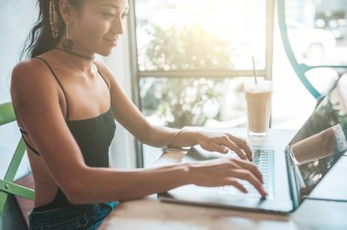 Kafede dizüstü bilgisayarı ve kahvesiyle çalışan Asyalı kadın