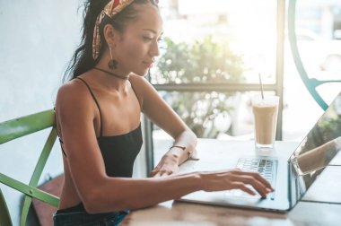 Kafede dizüstü bilgisayarı ve kahvesiyle çalışan Asyalı kadın