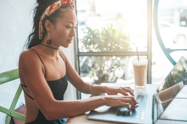 Kafede dizüstü bilgisayarı ve kahvesiyle çalışan Asyalı kadın