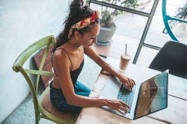 Kafede dizüstü bilgisayarı ve kahvesiyle çalışan Asyalı kadın