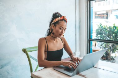 Kafede dizüstü bilgisayarı ve kahvesiyle çalışan Asyalı kadın