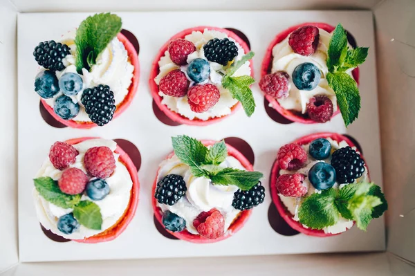 Cupcakes decorated with cream, berries and miny in box.