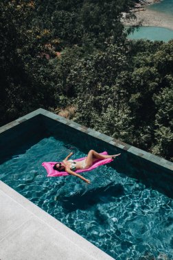 Bikinili seksi kadın yüzme havuzunda yaz güneşinin tadını çıkarıyor.