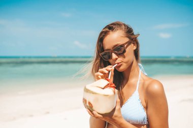 Tropikal plajda hindistan cevizi suyu içen genç güzel kadın