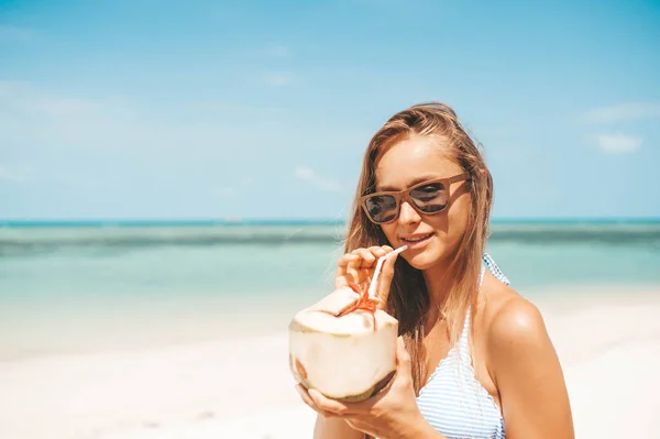Νεαρή όμορφη γυναίκα πίνοντας νερό καρύδας σε τροπική παραλία — Φωτογραφία Αρχείου