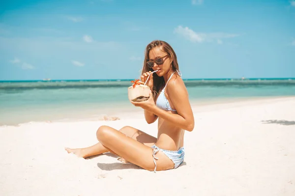 Молода красива жінка п'є кокосову воду на тропічному пляжі — стокове фото