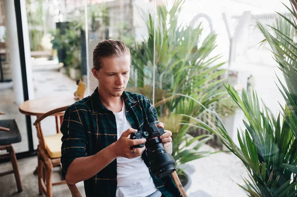 Fotografer kreatif memegang kamera profesional, duduk di kafe dengan laptop . — Stok Foto