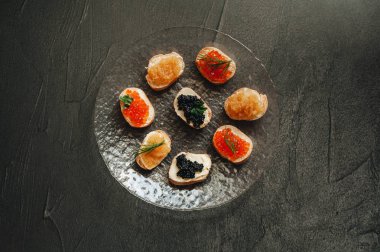 Şeffaf plaka üzerinde kırmızı somon havyar, mersin balığı siyah havyar ve pike havyar ile Sandviçler