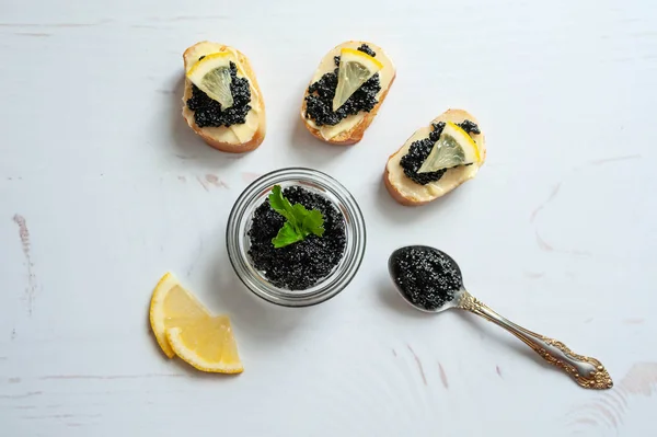 Frasco de caviar de esturjão preto e canapés com caviar no fundo branco — Fotografia de Stock
