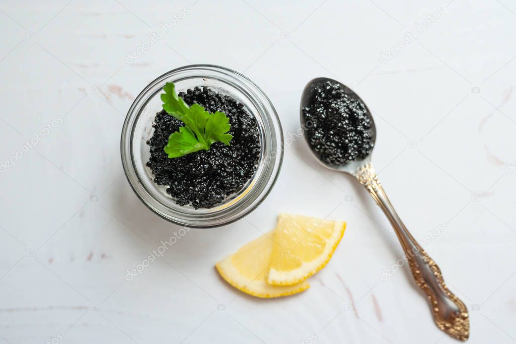 Jar of black sturgeon caviar and spoon with caviar on the white background
