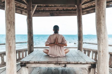 Genç kadın plajda ahşap çardak yoga yapıyor