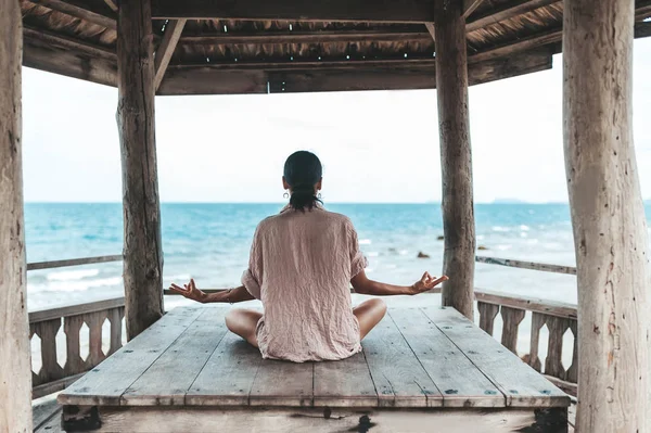 Young woman doing yoga in the wooden gazebo at the beach — Stock Photo, Image