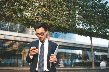 Arka planda şehir manzarası ile açık havada duran tam takım elbiseli modern işadamı