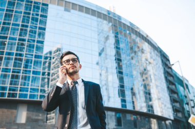 Arka planda şehir manzarası ile açık havada duran tam takım elbiseli modern işadamı