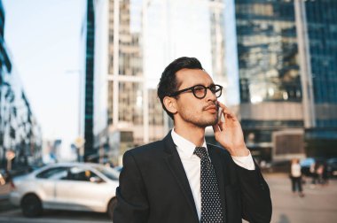 Arka planda şehir manzarası ile açık havada duran tam takım elbiseli modern işadamı