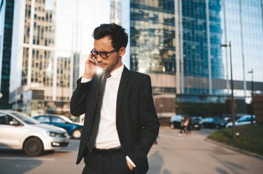 Arka planda şehir manzarası ile açık havada duran tam takım elbiseli modern işadamı