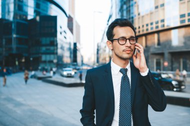 Arka planda şehir manzarası ile açık havada duran tam takım elbiseli modern işadamı