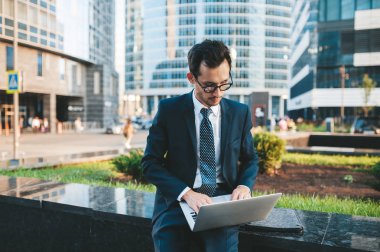 Arka planda şehir manzarası ile açık havada duran tam takım elbiseli modern işadamı