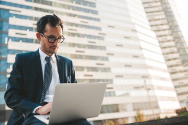 Arka planda şehir manzarası ile açık havada duran tam takım elbiseli modern işadamı