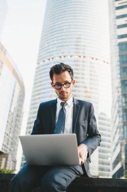 Arka planda şehir manzarası ile açık havada duran tam takım elbiseli modern işadamı