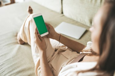 Evdeki kanepede uzanmış telefon kullanan genç sarışın kadın.