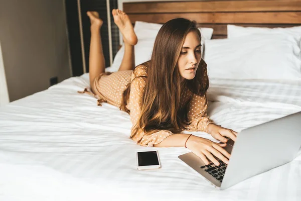 Жінка Довгим Волоссям Лежить Ліжку Схрещеними Ногами Робочим Ноутбуком Спальні — стокове фото