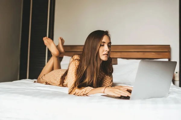 Жінка Довгим Волоссям Лежить Ліжку Схрещеними Ногами Робочим Ноутбуком Спальні — стокове фото