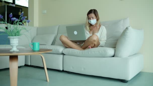 女性は隔離と隔離中に自宅から働く医療用保護マスクを着用しています. — ストック動画