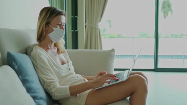 Woman wears medical protective mask working from home at the computer during self-isolation and quarantine. Royalty Free Stock Footage