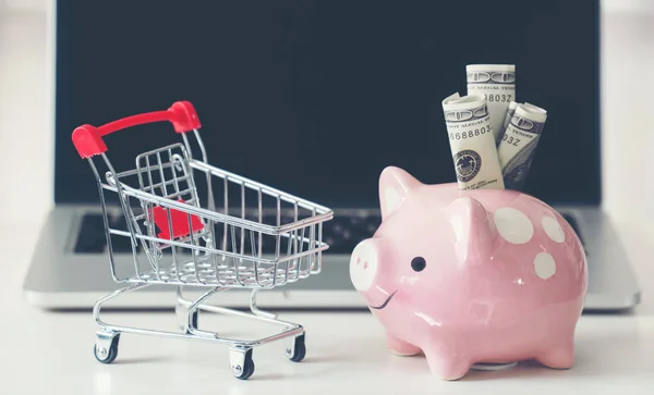 Shopping cart and piggy bank with laptop on the desk — Stock Photo, Image