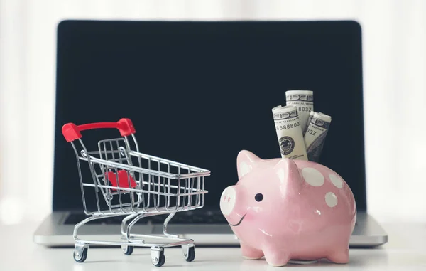 Shopping cart and piggy bank with laptop on the desk — Stock Photo, Image