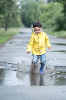 Su birikintisine oynarken küçük çocuk yağmurluk ve lastik çizmeler