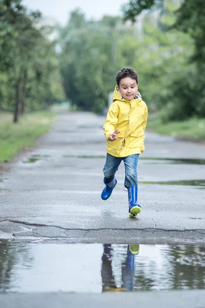 レインコート ゴムで小さな男の子は 水たまりで遊んでブーツします — ストック写真