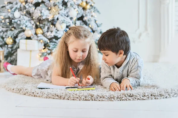 boy and girl write letter to Santa Claus near christmas tree. Merry Christmas and Happy Holidays. children lie on floor