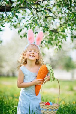 Paskalya yumurtaları ve bahçesinde tavşan kulakları olan sevimli, komik bir kız. Paskalya konsepti. Paskalya yumurtası avında gülen çocuk. Sepet dolusu yumurta ve bahar konseptiyle parkta bir çocuk.