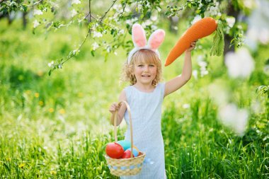 Paskalya yumurtaları ve bahçesinde tavşan kulakları olan sevimli, komik bir kız. Paskalya konsepti. Paskalya yumurtası avında gülen çocuk. Sepet dolusu yumurta ve bahar konseptiyle parkta bir çocuk.