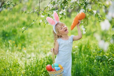Paskalya yumurtaları ve bahçesinde tavşan kulakları olan sevimli, komik bir kız. Paskalya konsepti. Paskalya yumurtası avında gülen çocuk. Sepet dolusu yumurta ve bahar konseptiyle parkta bir çocuk.