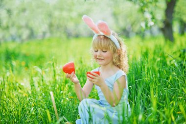 Paskalya yumurtaları ve bahçesinde tavşan kulakları olan sevimli, komik bir kız. Paskalya konsepti. Paskalya yumurtası avında gülen çocuk. Sepet dolusu yumurta ve bahar konseptiyle parkta bir çocuk.