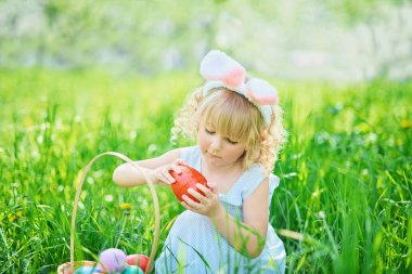 Paskalya yumurtaları ve bahçesinde tavşan kulakları olan sevimli, komik bir kız. Paskalya konsepti. Paskalya yumurtası avında gülen çocuk. Sepet dolusu yumurta ve bahar konseptiyle parkta bir çocuk.
