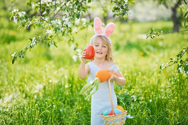 Paskalya yumurtaları ve bahçesinde tavşan kulakları olan sevimli, komik bir kız. Paskalya konsepti. Paskalya yumurtası avında gülen çocuk. Sepet dolusu yumurta ve bahar konseptiyle parkta bir çocuk.