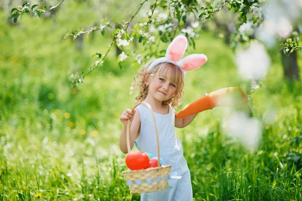 Paskalya yumurtaları ve bahçesinde tavşan kulakları olan sevimli, komik bir kız. Paskalya konsepti. Paskalya yumurtası avında gülen çocuk. Sepet dolusu yumurta ve bahar konseptiyle parkta bir çocuk.