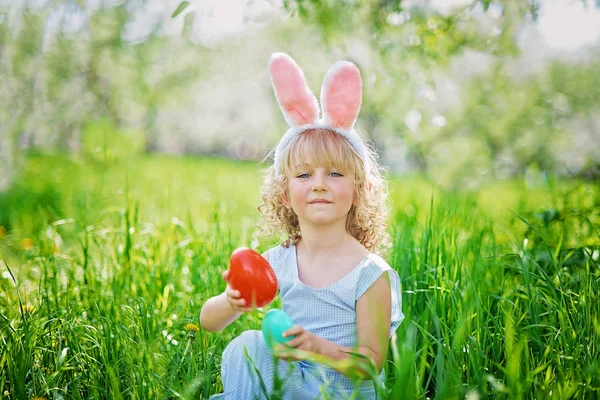Paskalya yumurtaları ve bahçesinde tavşan kulakları olan sevimli, komik bir kız. Paskalya konsepti. Paskalya yumurtası avında gülen çocuk. Sepet dolusu yumurta ve bahar konseptiyle parkta bir çocuk.